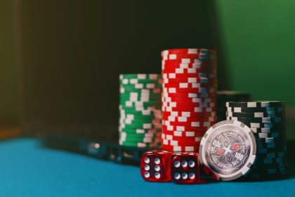 Fichas de cassino e dados sobre uma mesa, ao lado de um laptop usado para apostas online