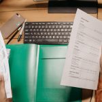 Mãos analisam planilhas financeiras sobre uma mesa com teclado e materiais de escritório.