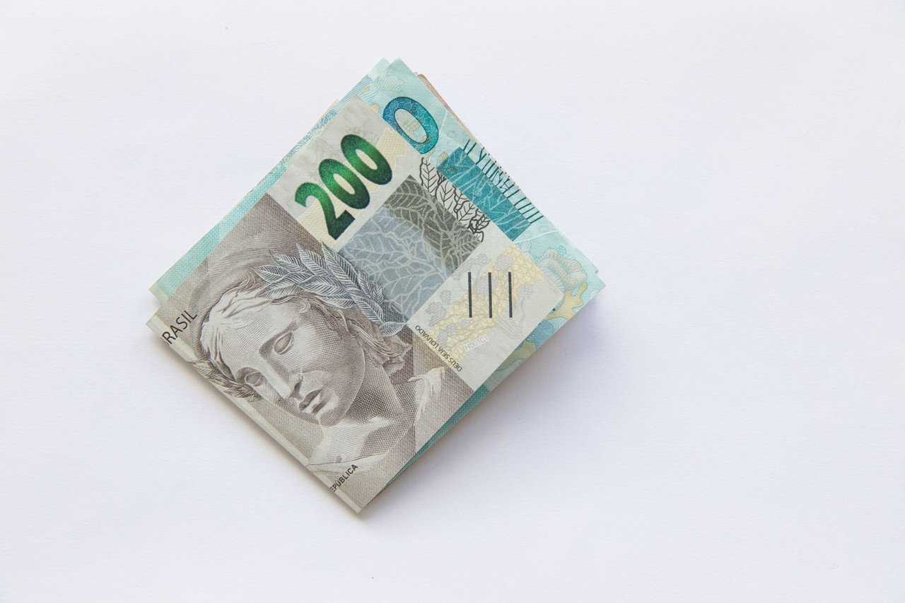 Pilha de cédulas de 200 reais brasileiras sobre uma superfície branca.