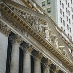 Fachada da Bolsa de Nova York, em Manhattan, com colunas clássicas e bandeiras dos Estados Unidos