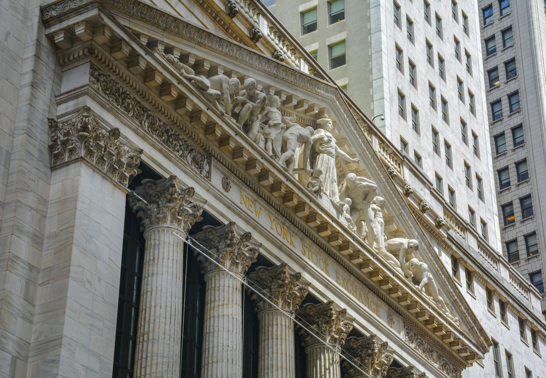 Fachada da Bolsa de Nova York, em Manhattan, com colunas clássicas e bandeiras dos Estados Unidos