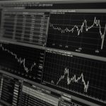Monitores exibem gráficos e dados de mercado financeiro em preto e branco.