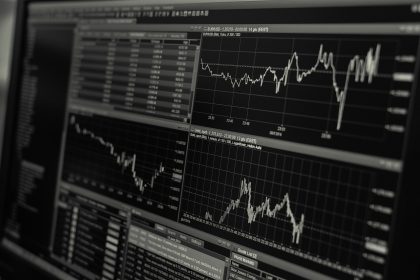 Monitores exibem gráficos e dados de mercado financeiro em preto e branco.