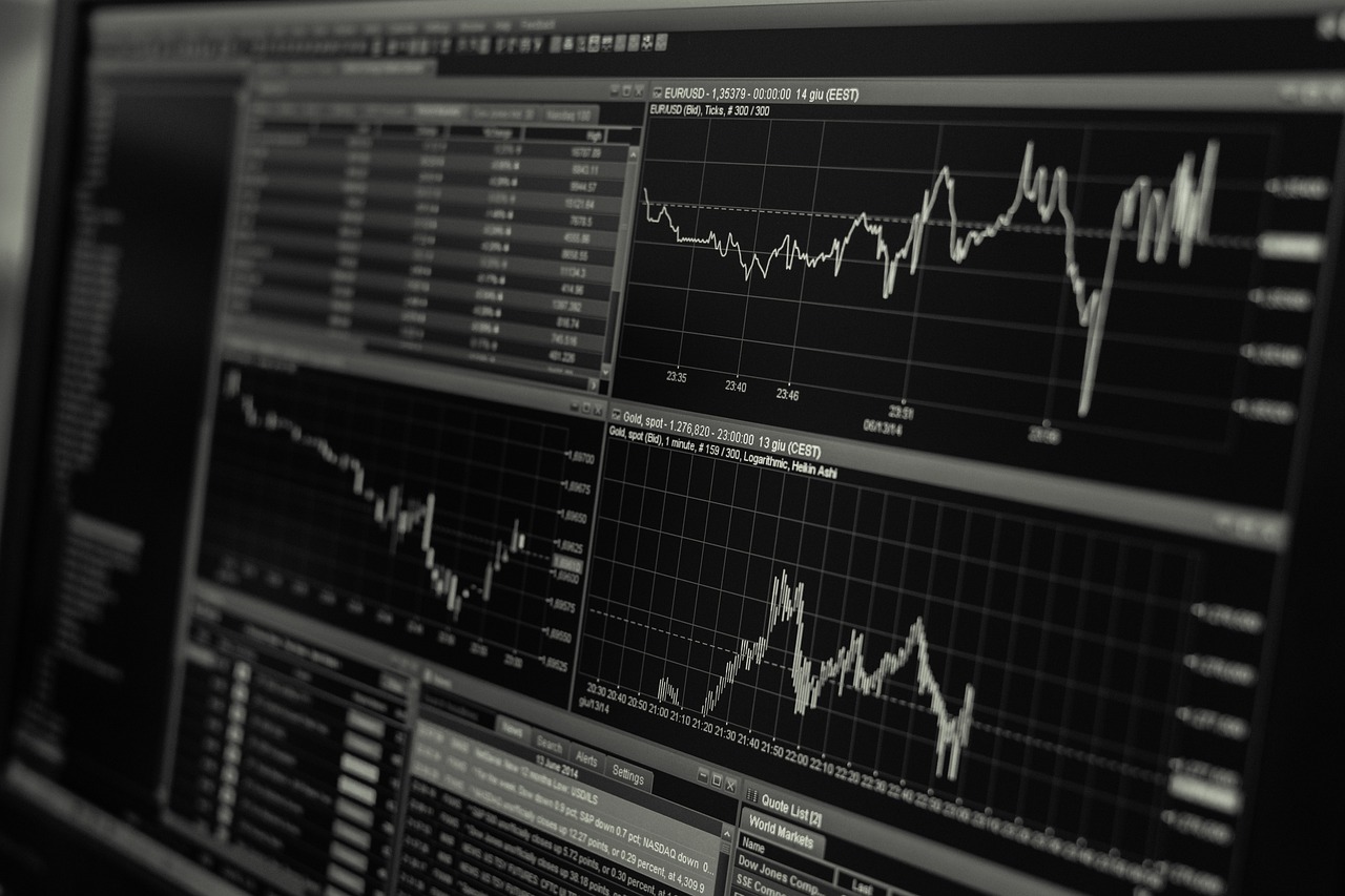 Monitores exibem gráficos e dados de mercado financeiro em preto e branco.